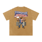 Beige t-shirt with a graphic of a man in chains wearing an American flag shirt and 'Foundation of Freedom' text on a white background.