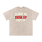 Beige t-shirt with text 'Clock In Drink Up Shut Up' on a white background